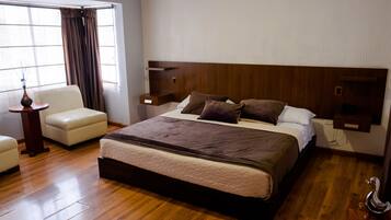 Une chambre à coucher avec un grand lit, une chaise, une table de chevet et une fenêtre avec des rideaux.