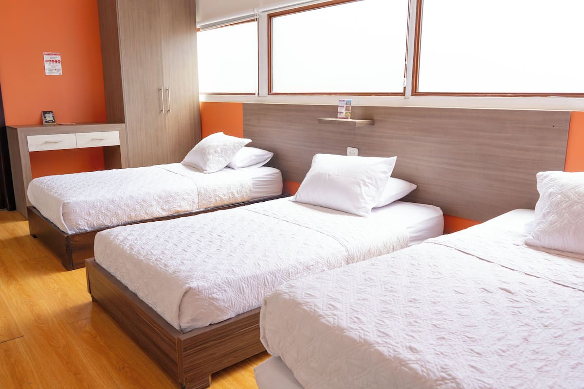 A hotel room with two single beds, a wooden wardrobe, a desk with a chair, and a window with a view.