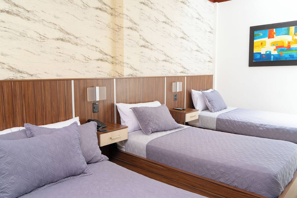 A hotel room with two beds, marble walls, wooden headboard, bedside tables, and a colorful painting.