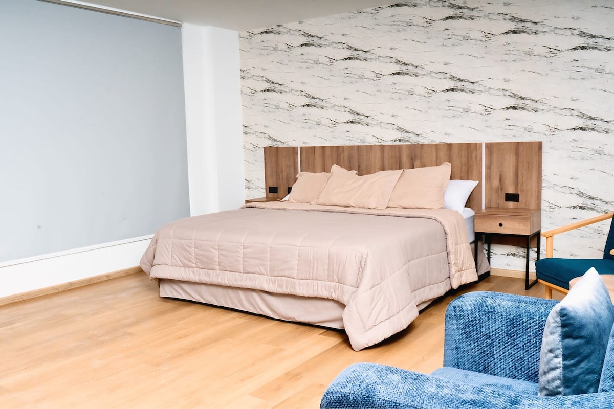 A bedroom with a bed, a nightstand, a chair, and a marble-patterned wall.