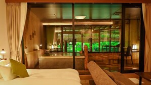 A hotel room with a bed, a bench, a table, and a view of a garden through large glass doors. - Kutsurogijuku Chiyotaki (Aizuwakamatsu)