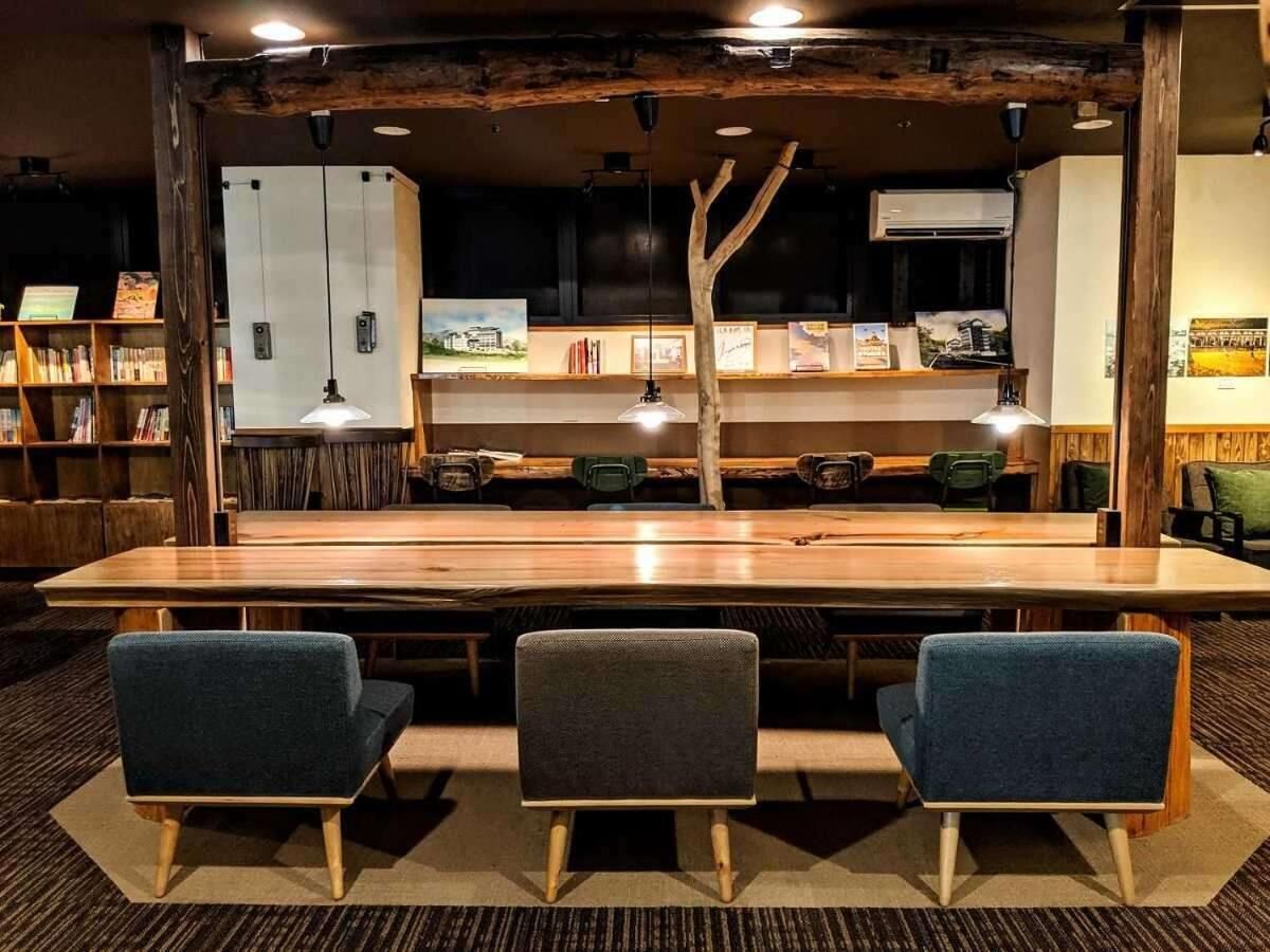 Un restaurante con una larga mesa de madera, tres sillas tapizadas y decoración rústica con vigas a la vista y una lámpara colgante.