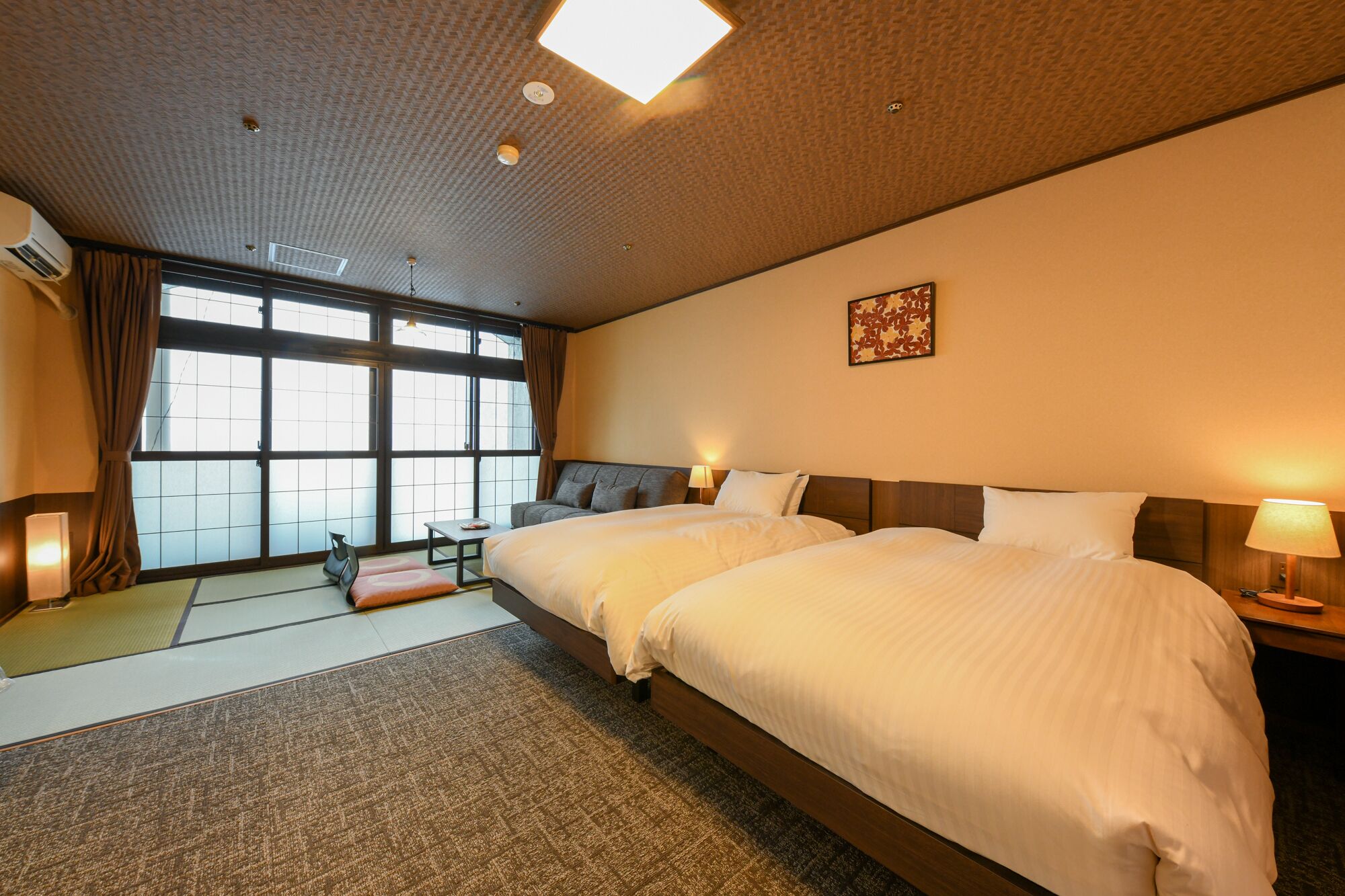 A hotel room with two beds, a large window, a tatami mat, and a traditional Japanese artwork.