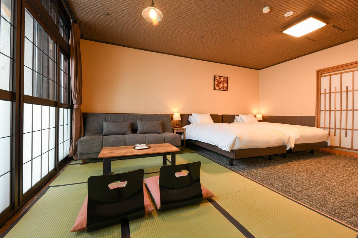 A hotel room with a sofa, two beds, a wooden table, and tatami mats.
