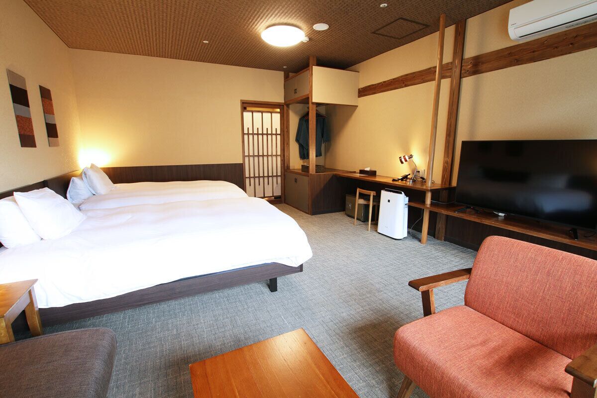 A hotel room with a large bed, a TV, a desk, and a chair.