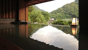A serene indoor pool with a wooden ceiling and a view of lush green mountains and a building in the distance. - Kutsurogijuku Chiyotaki (Aizuwakamatsu)