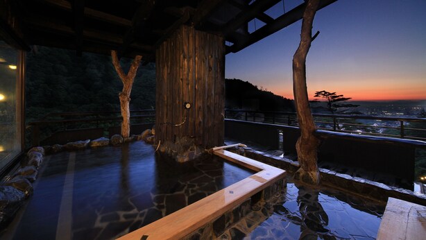 A wooden hot spring bath with stone flooring and a view of the city at sunset. - Kutsurogijuku Chiyotaki (Aizuwakamatsu)