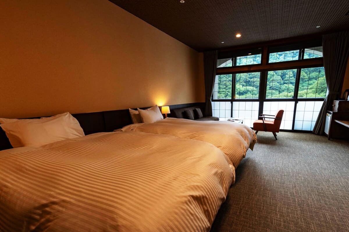 A hotel room with a large bed, a chair, and a view of greenery through the window.