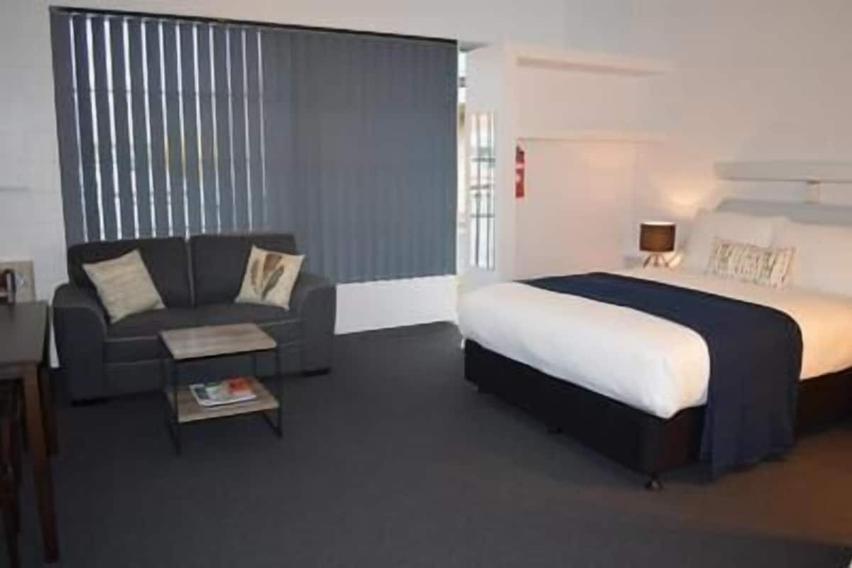 Una habitación de hotel con cama, sofá, mesa de centro y ventana con persianas.