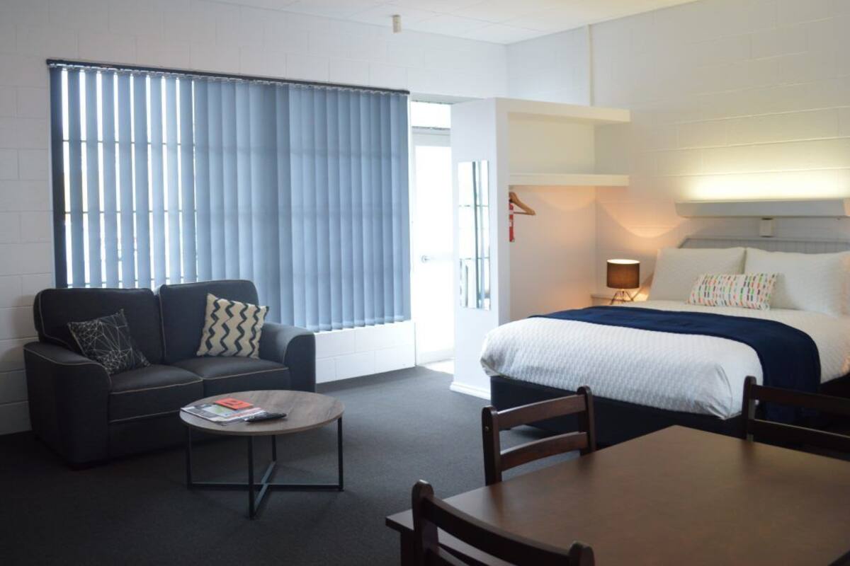 Una habitación de hotel moderna con una cama grande, un sofá, una mesa de centro y una mesa de comedor.