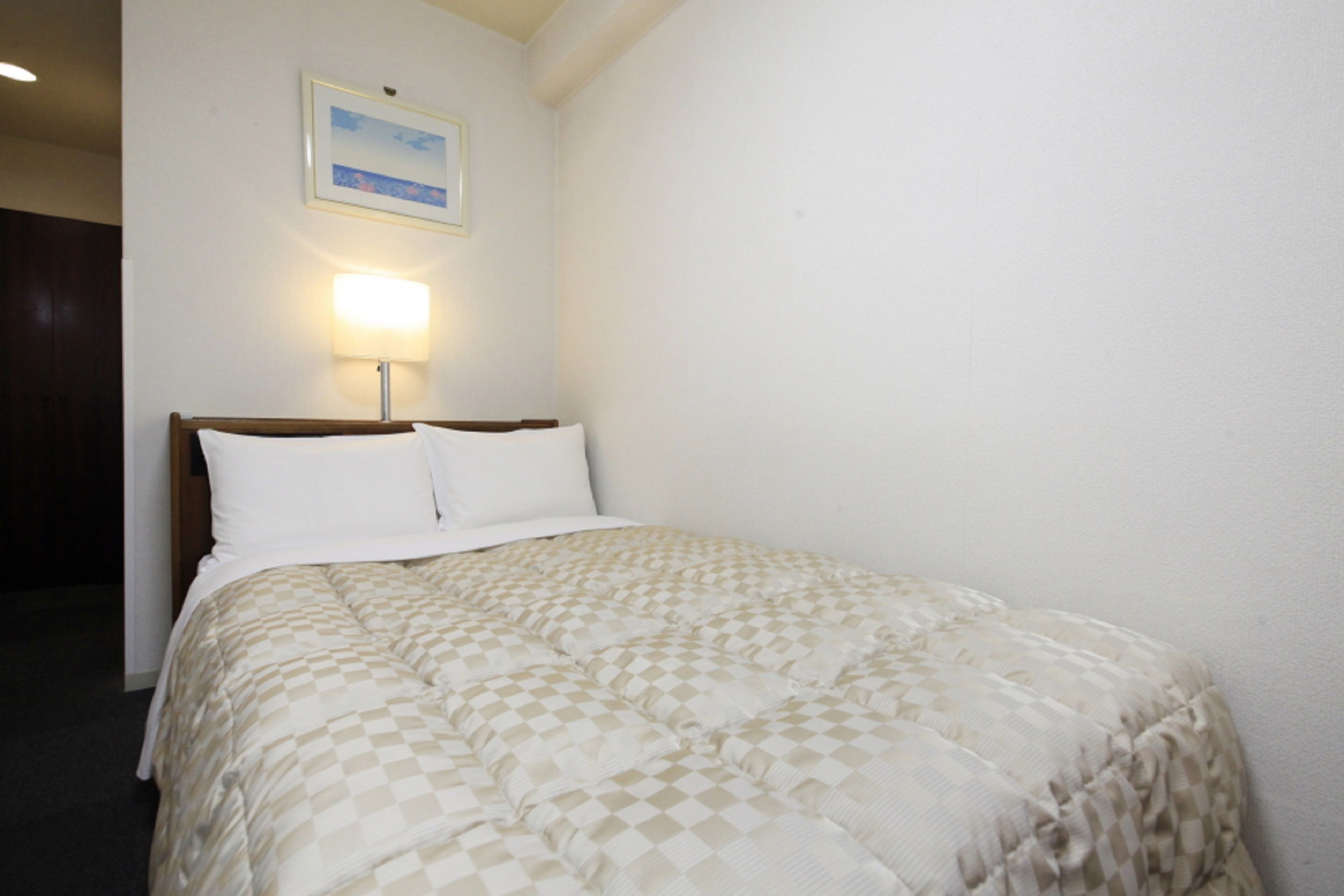 Una habitación de hotel con una cama, una mesita de noche, una lámpara y un cuadro en la pared.
