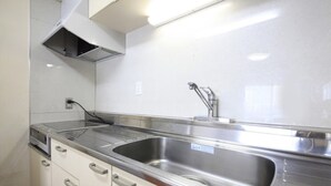 A kitchen with a stainless steel sink, white cabinets, and a microwave. - Shinjuku Urban Hotel (Tokyo)