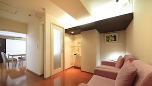A modern living room with a wooden floor, a sofa set, a small table, and a door leading to another room. - Shinjuku Urban Hotel (Tokyo)