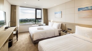 Une chambre d’hôtel avec deux lits, un bureau, une chaise, une fenêtre donnant sur un beau paysage et un tableau au mur.