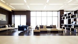 Un espace de détente moderne et bien éclairé, comprenant un canapé, des fauteuils, une petite table et une bibliothèque.