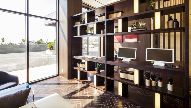 Un espace de bureau moderne doté de grandes fenêtres, d’un parquet disposé en chevrons et d’une étagère en bois sur laquelle sont posés des écrans et des objets décoratifs.