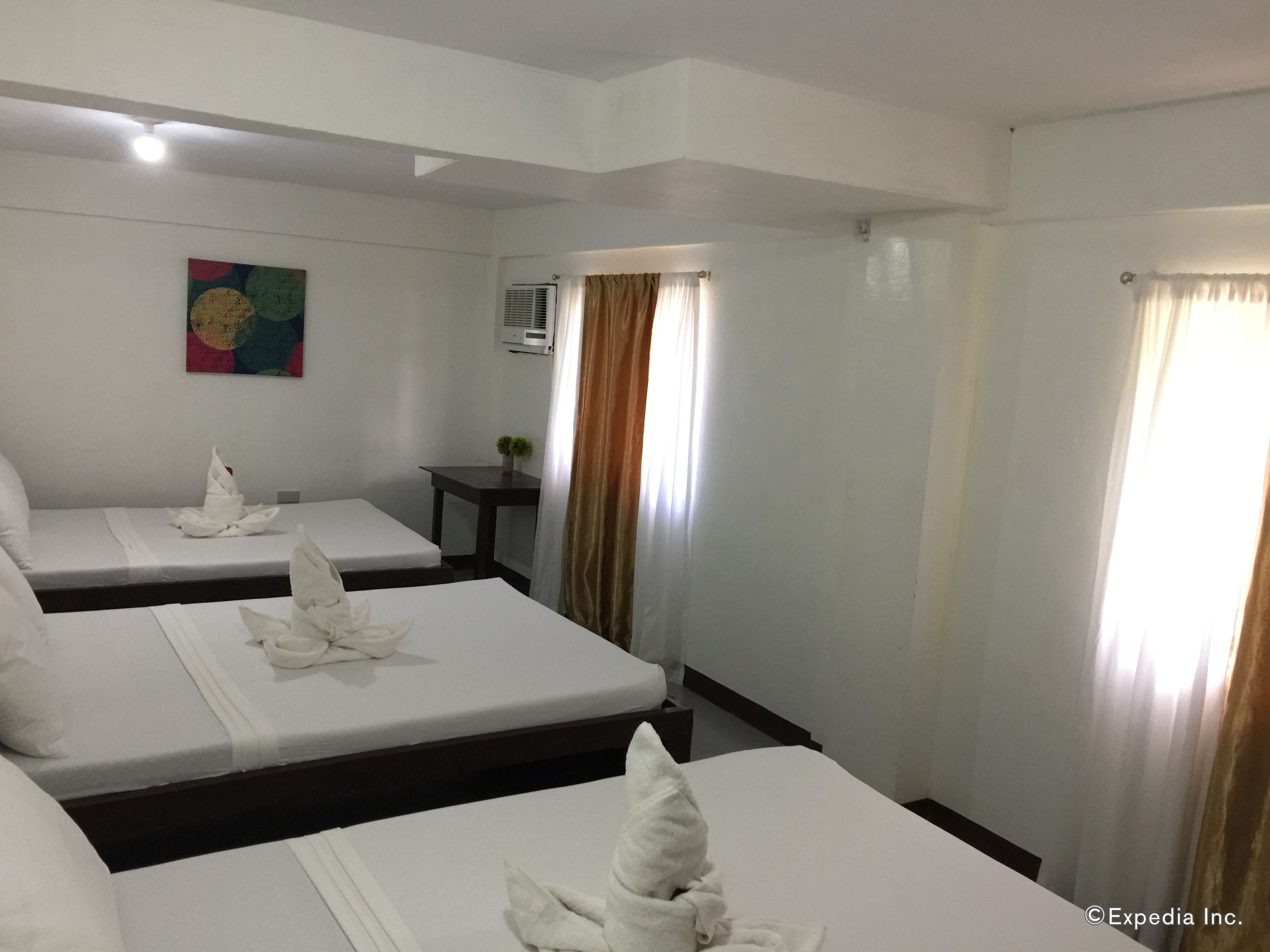 Habitación de hotel con dos camas, cada una con toallas blancas dobladas con cuidado, una mesita con planta en maceta y un cuadro colorido en la pared.