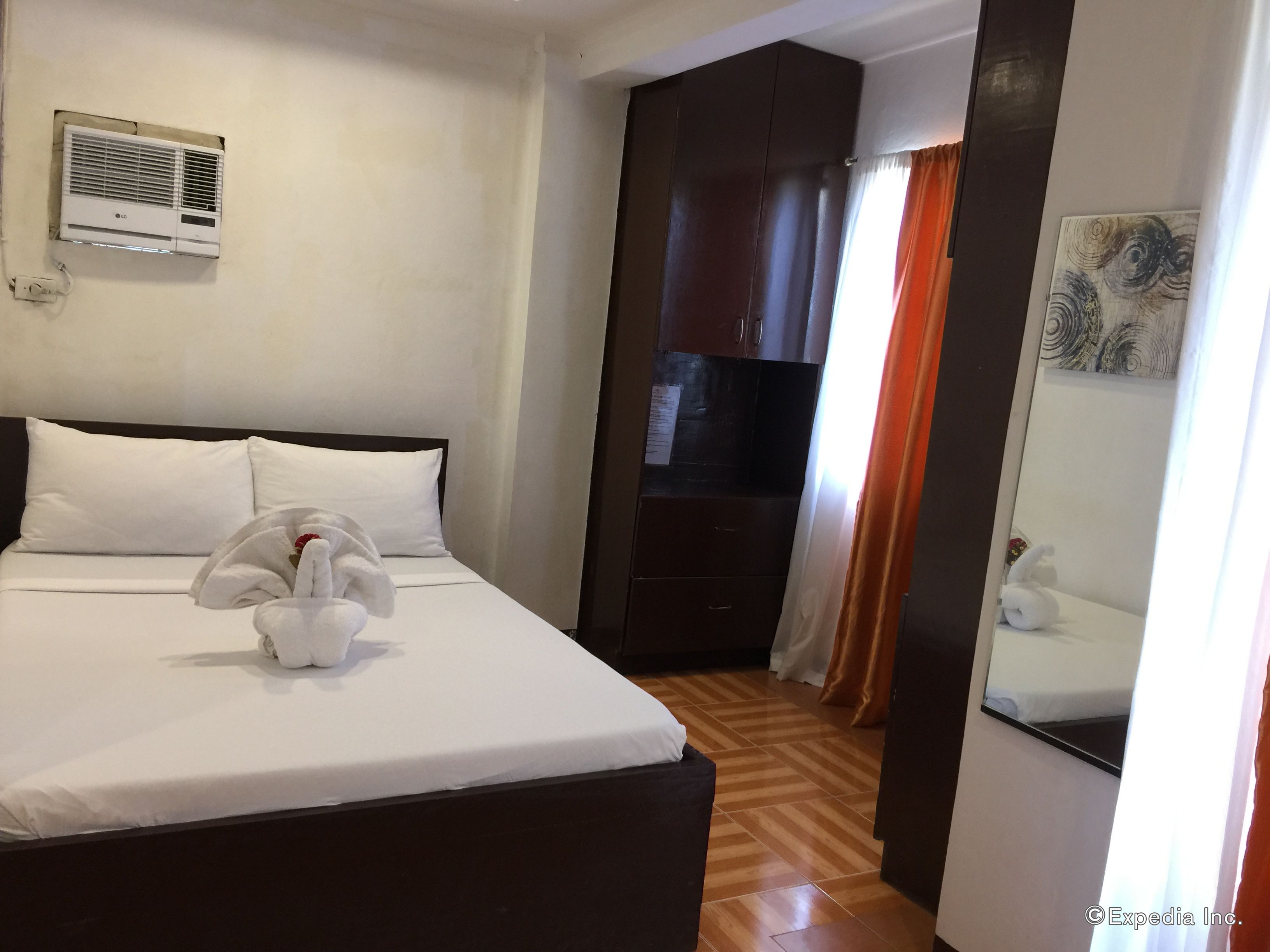 Una habitación de hotel con cama, aire acondicionado de pared, suelo de madera y un armario oscuro.