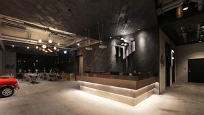 Et moderne receptionområde med en central disk, synlige ventilationsrør og en rød bil i baggrunden.