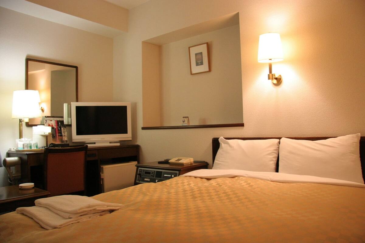 A hotel room with a bed, a desk with a television, a lamp, and a mirror.