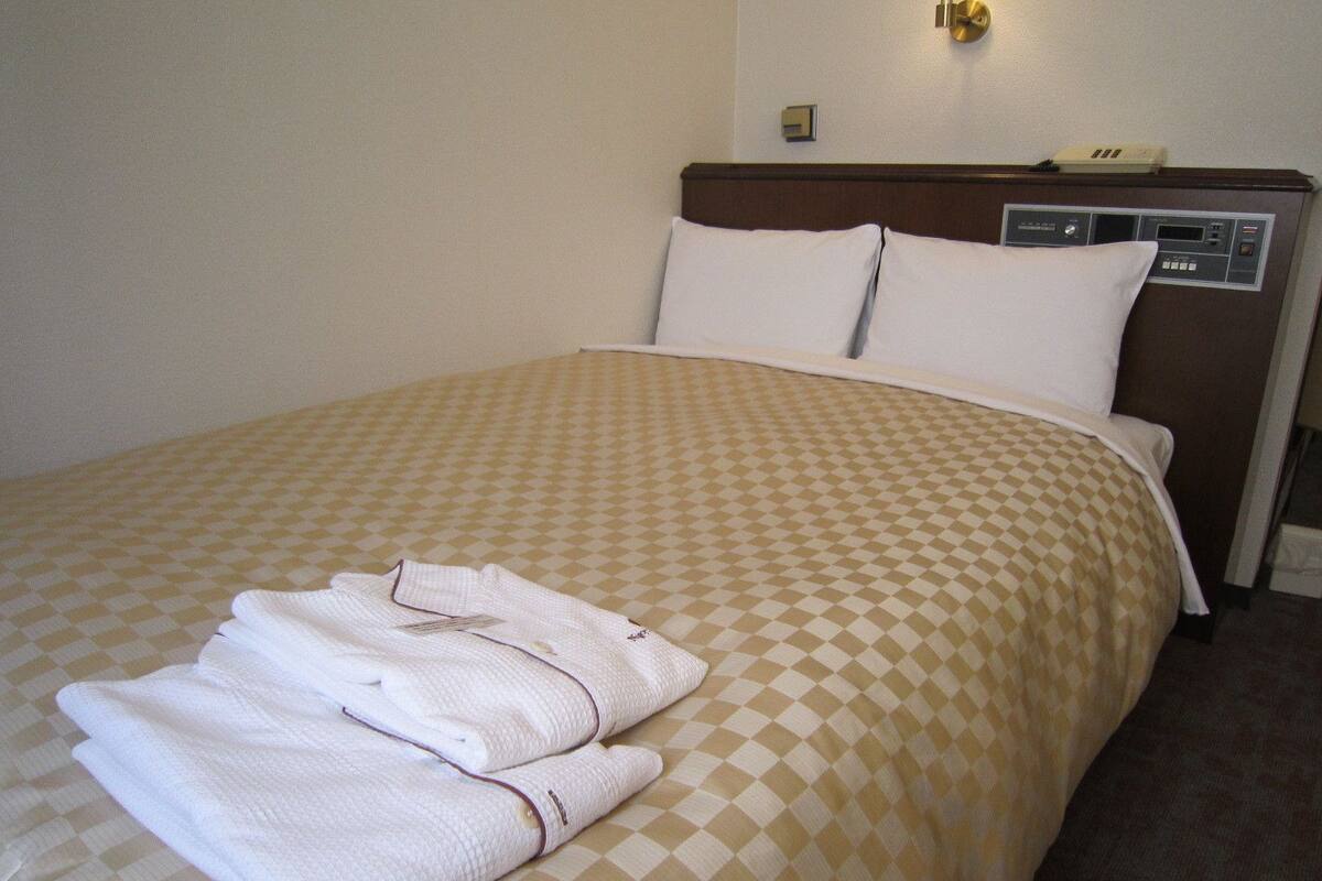 A hotel room with a checkered bedspread, two pillows, and a folded towel on the bed.