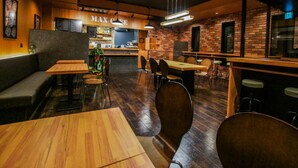 A restaurant interior with wooden tables and chairs, a bar area, and a brick wall. - HOTEL LiVEMAX Minamihashimoto Ekimae (Sagamihara)