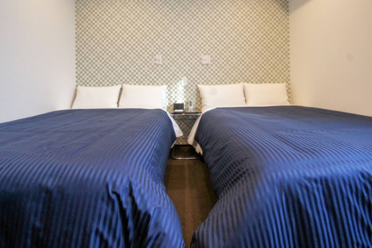 A hotel room with two single beds, a small bedside table, and a checkered wall pattern.