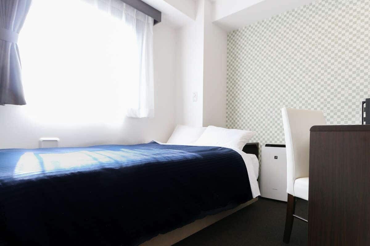 A hotel room with a bed, a chair, a desk, and a window with curtains.