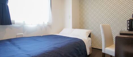 Una habitación de hotel con cama, una silla, un escritorio con computadora y una ventana con cortinas.