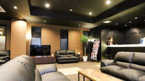 A modern hotel lobby with leather sofas, a flat-screen TV, a reception desk, and a plant. - HOTEL LiVEMAX Minamihashimoto Ekimae (Sagamihara)