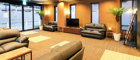 A modern lounge area with leather sofas, a flat-screen TV, and potted plants.