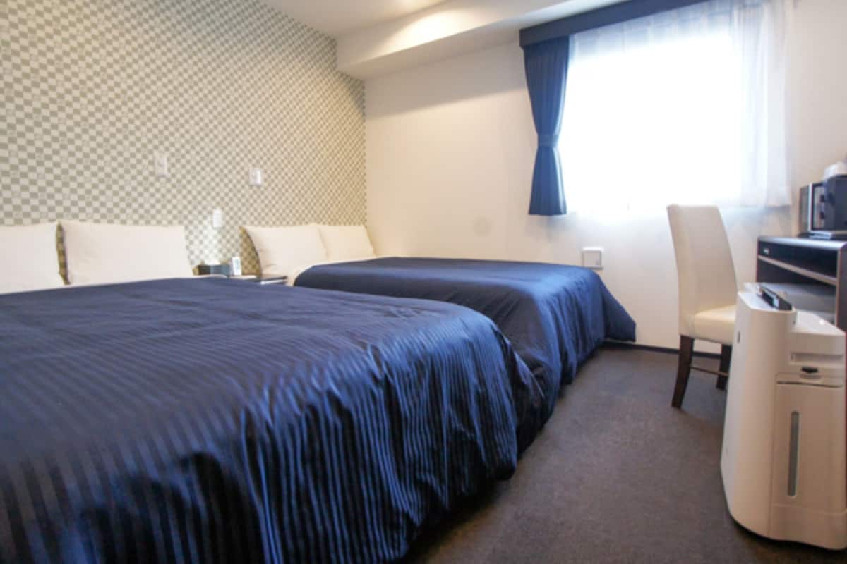 A hotel room with two beds, a desk with a computer, and a chair.