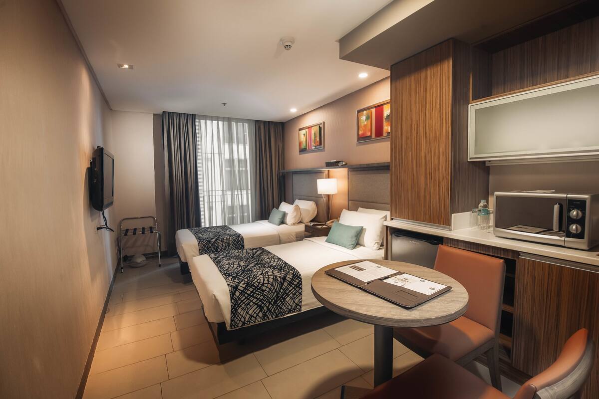 Una habitación de hotel con dos camas, una mesa de comedor, microondas y televisión.