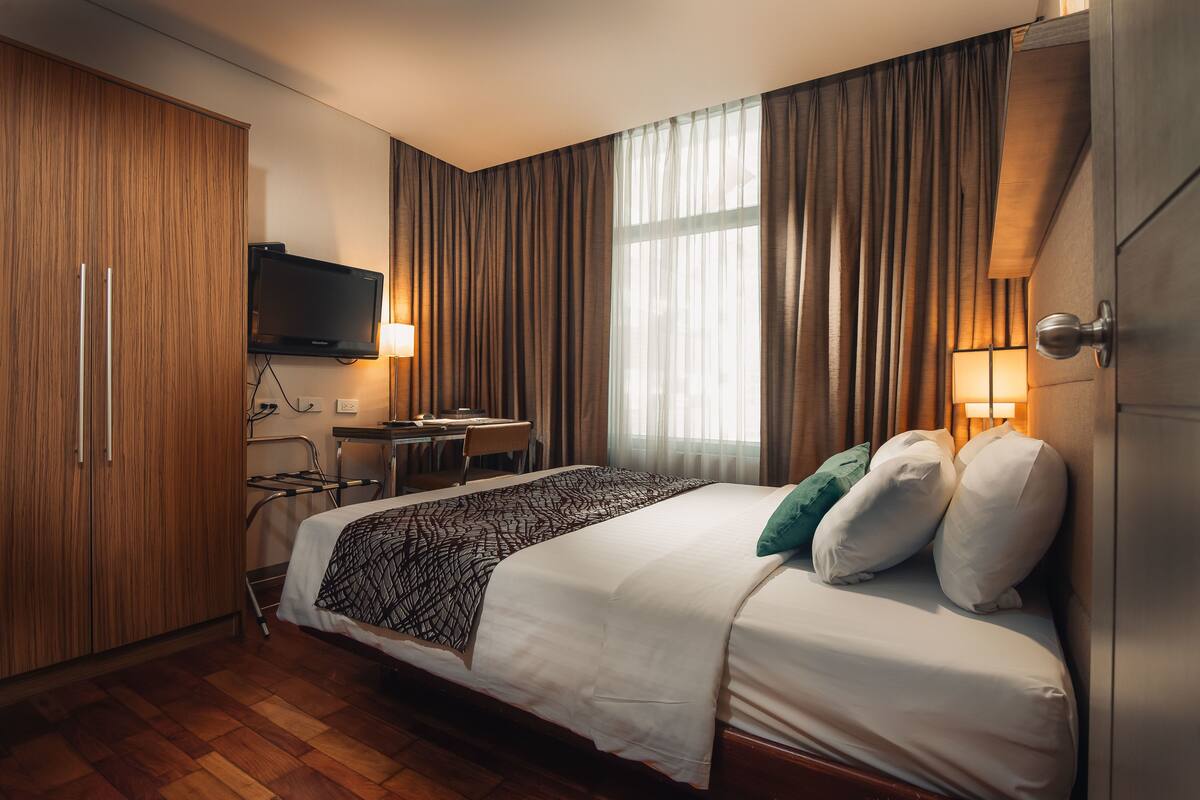 Una habitación de hotel con una cama, un escritorio, una silla, un televisor y cortinas.