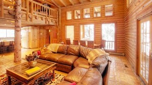 Interno di una baita in legno con un ampio divano in pelle, pavimento in legno e diverse finestre.