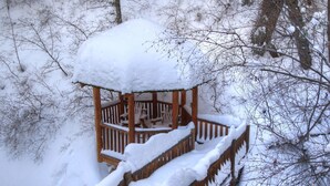 Un gazebo in legno ricoperto di neve, circondato da alberi.