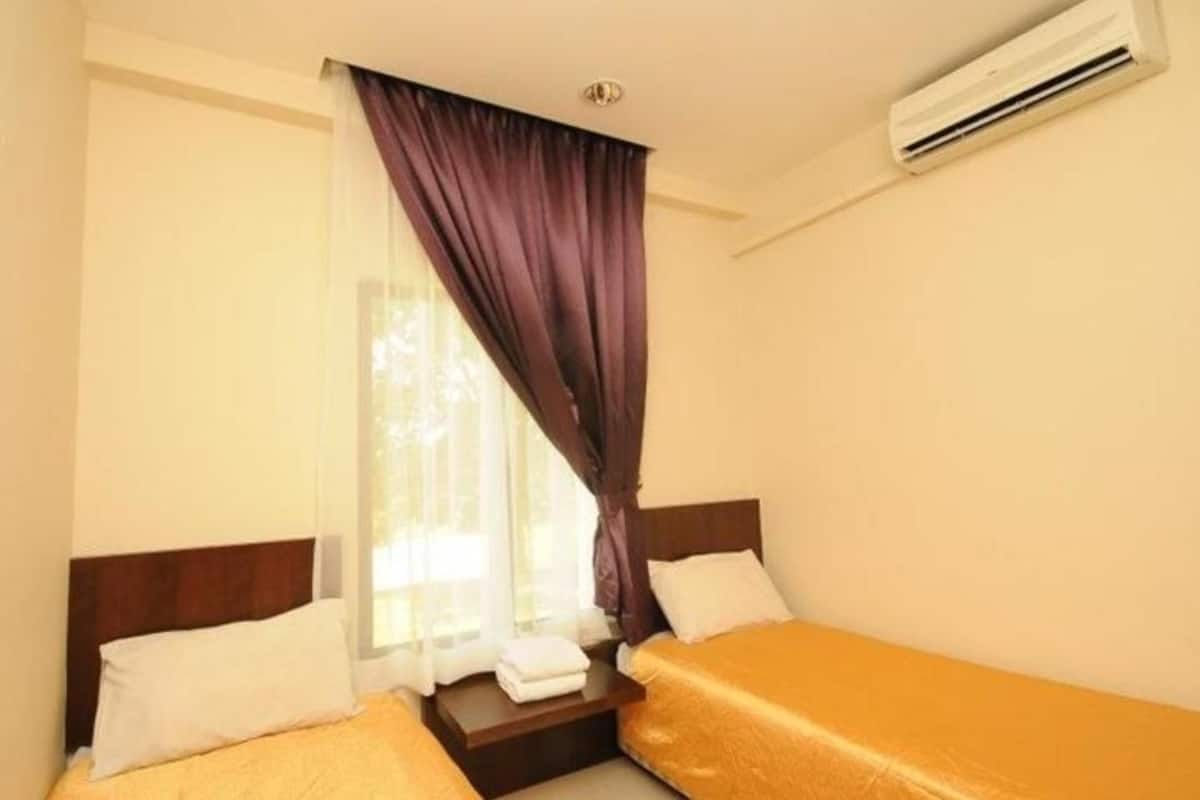 A hotel room with two single beds, a window with curtains, an air conditioning unit, and a small table with a towel.