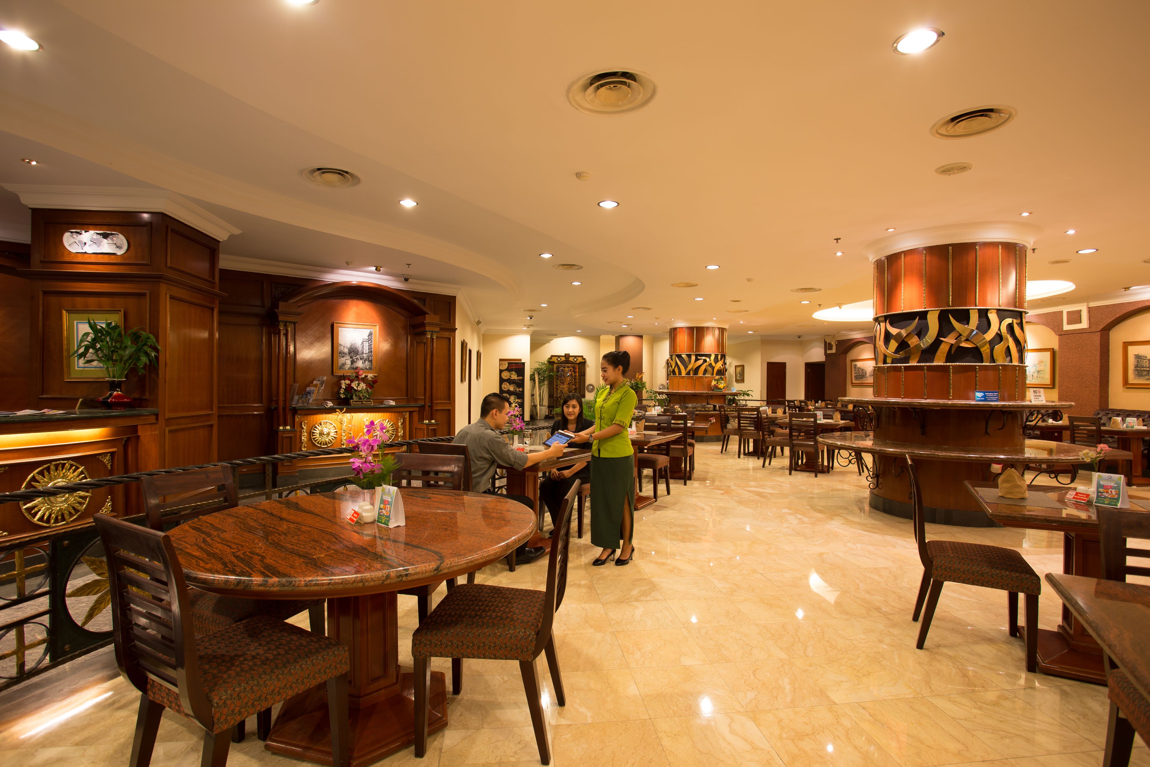 A spacious hotel lobby with wooden furniture, a reception desk, and a large decorative pillar.