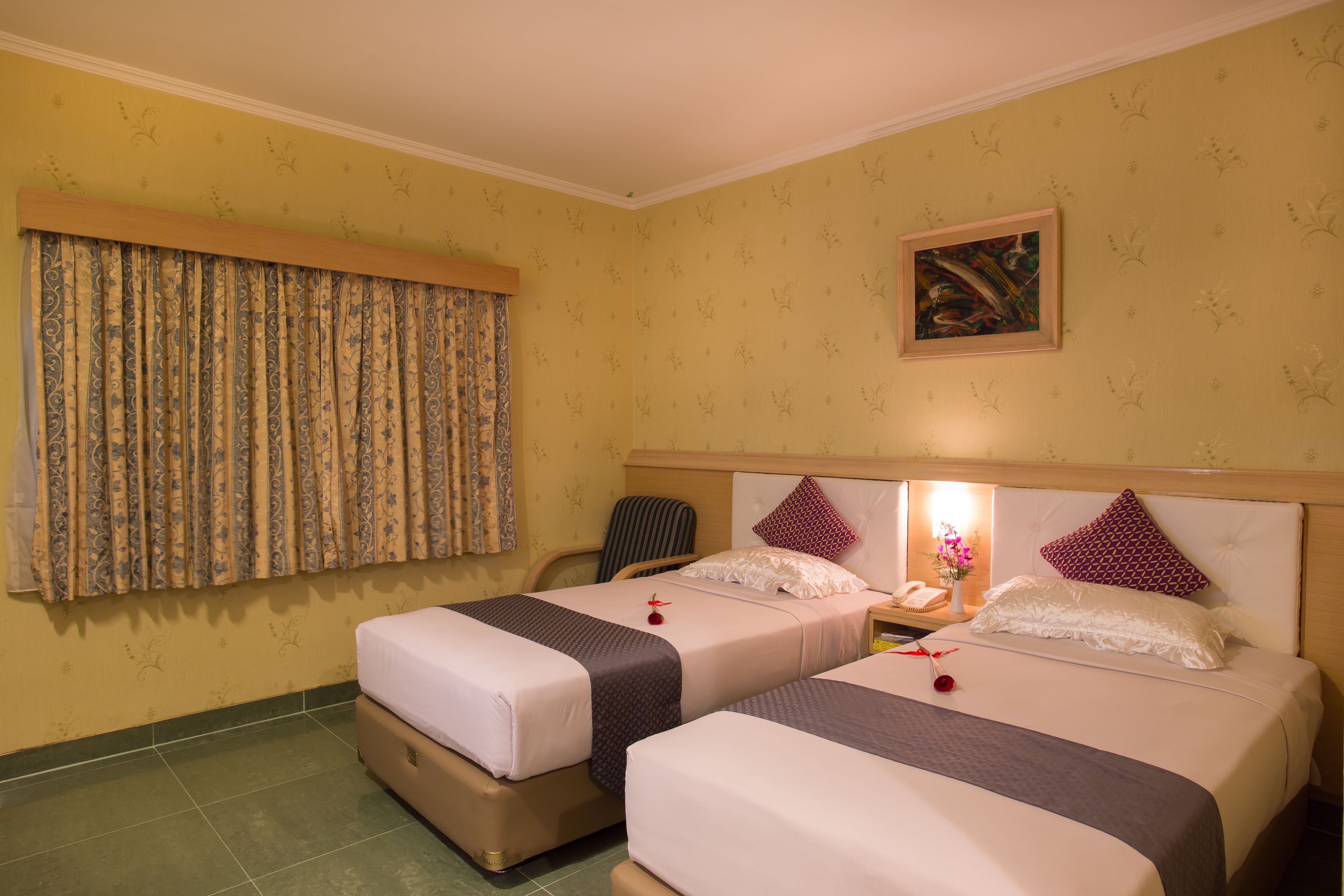 Una habitación de hotel con dos camas, una silla, una mesita de noche con lámpara y un cuadro en la pared.