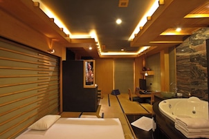 A modern hotel room with a bed, a desk, a large bathtub, and a bathroom with a marble wall.