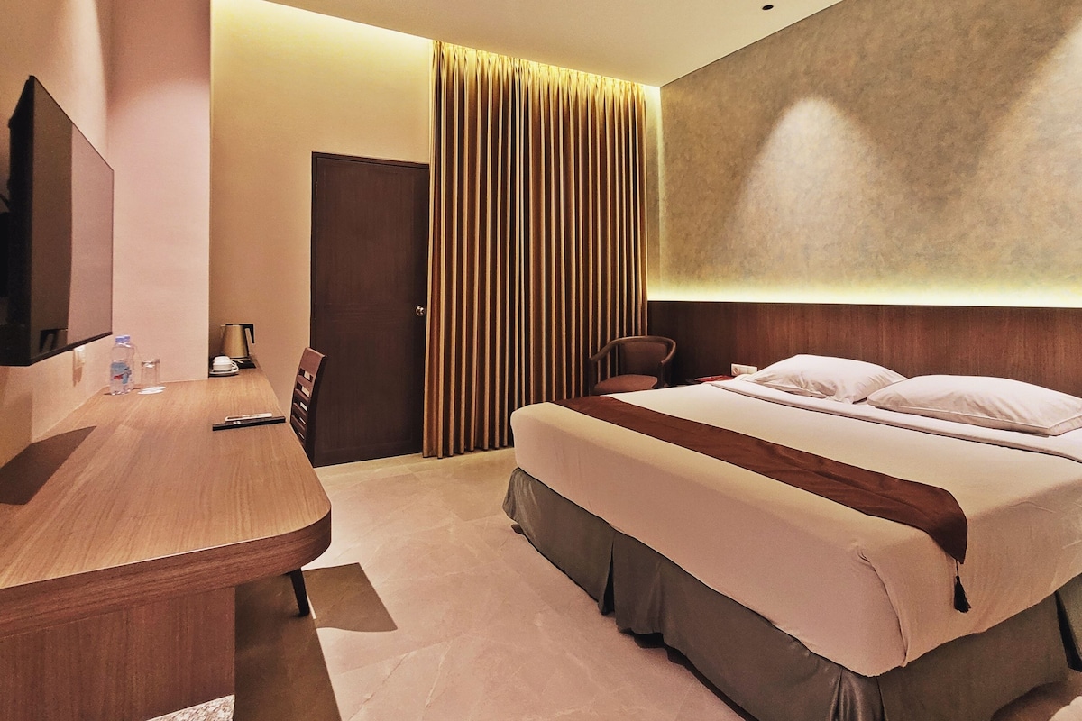 Quarto de hotel com cama, mesa de cabeceira, cadeira e televisão de tela plana.
