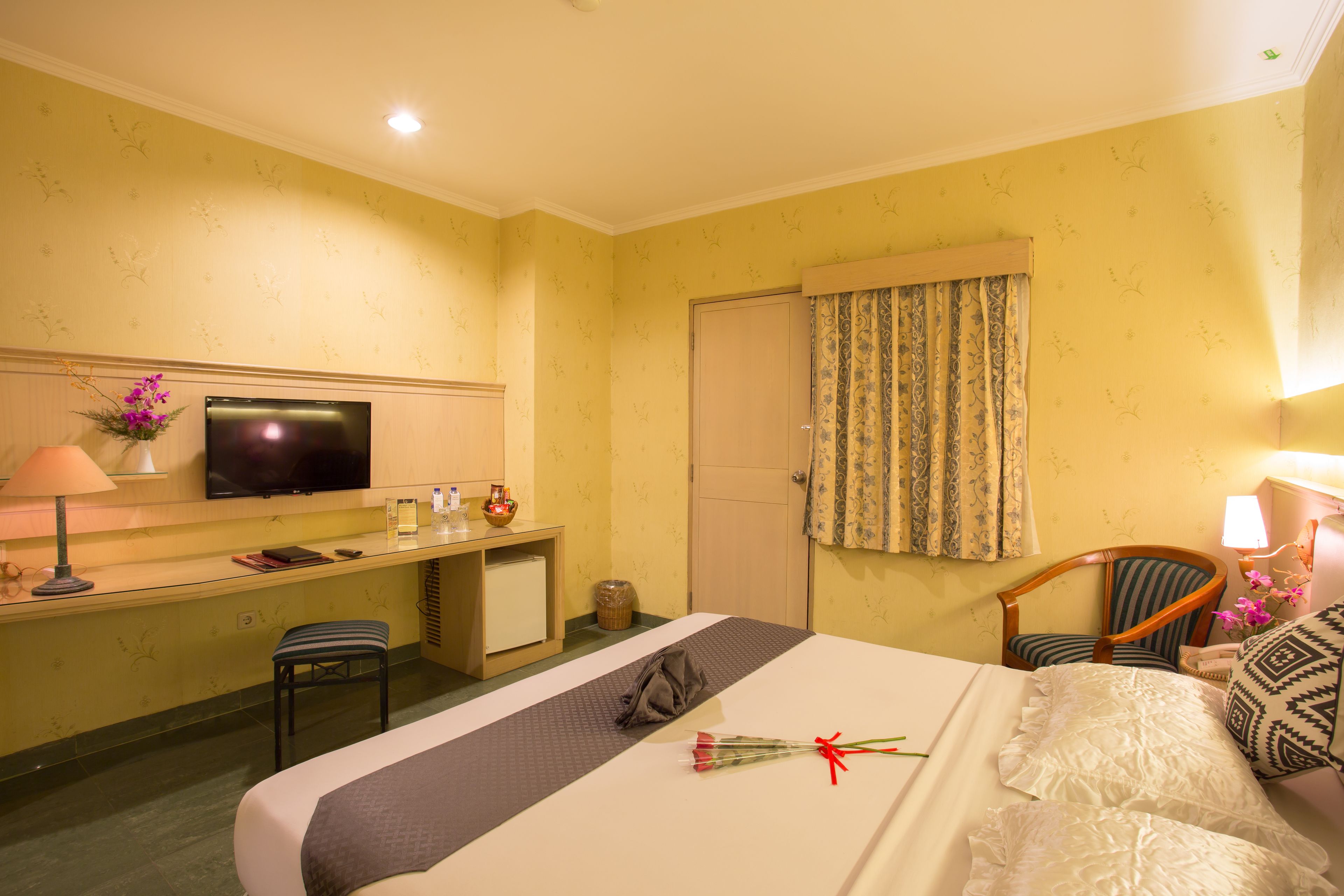 Habitación de hotel con cama, escritorio con televisor, silla y ventana con cortinas.