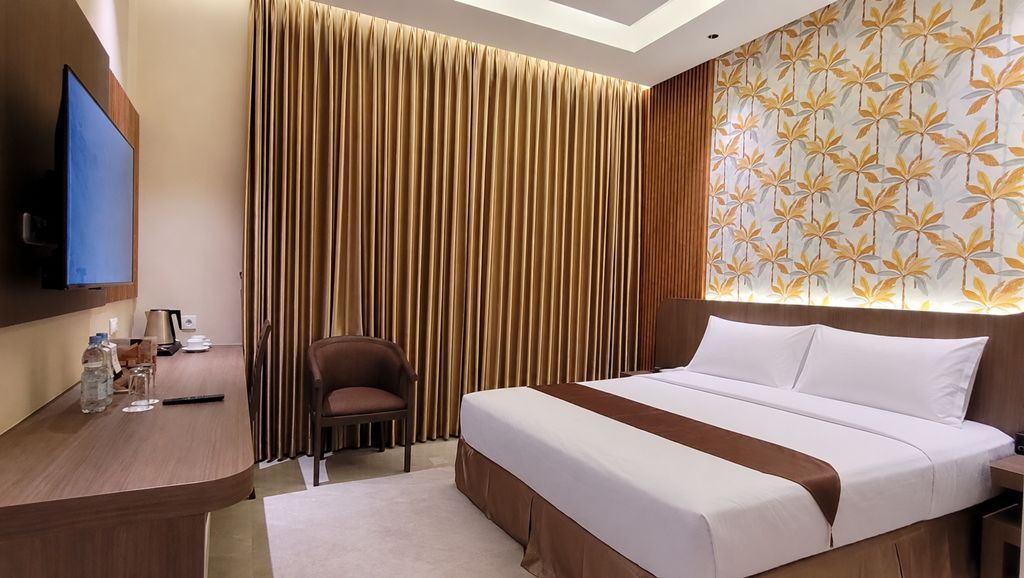 Ein Hotelzimmer mit Bett, Schreibtisch, Stuhl, Fernseher und Vorhang.