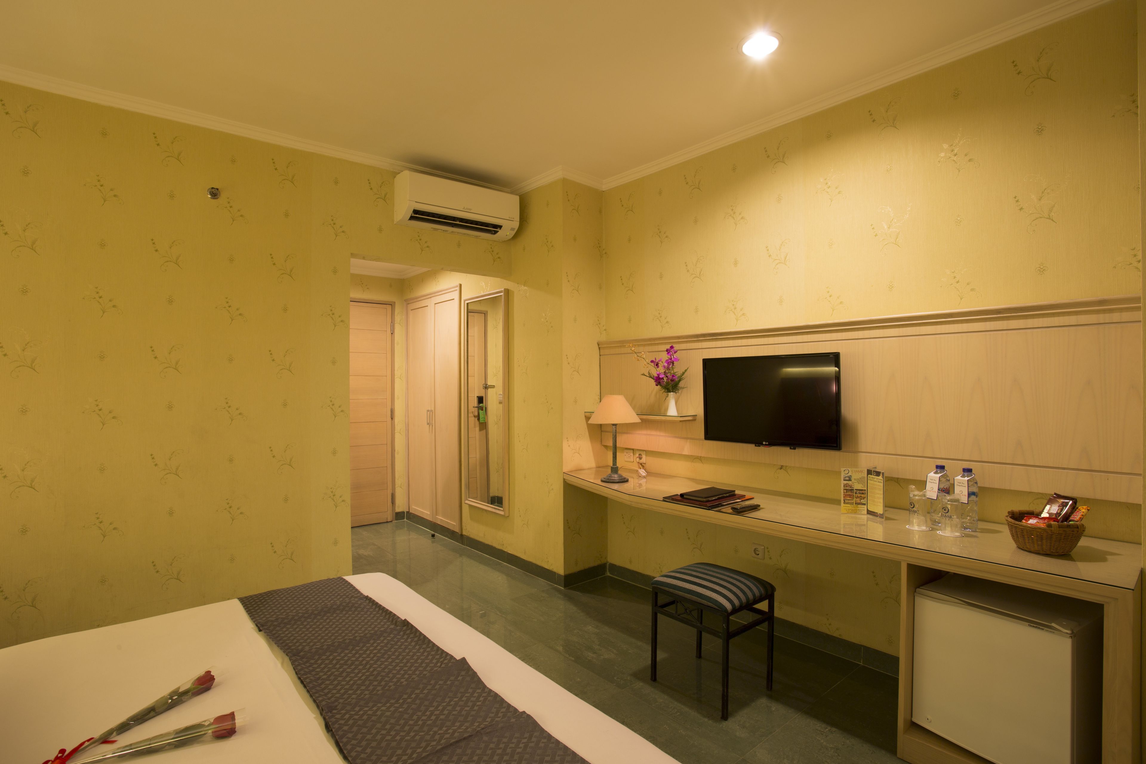 Een hotelkamer met een bed, een bureau, een televisie, een kleine koelkast en een badkamers deur.