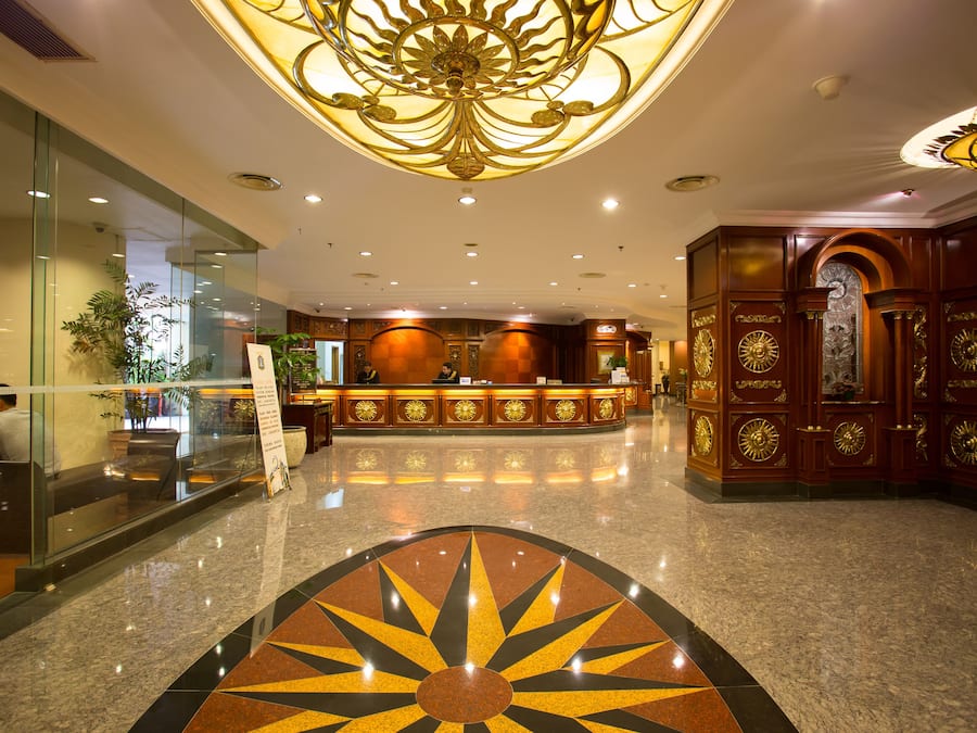 A hotel lobby with a reception desk, glass walls, and a decorative ceiling.