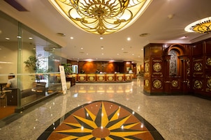 A hotel lobby with a reception desk, glass walls, and a decorative ceiling.