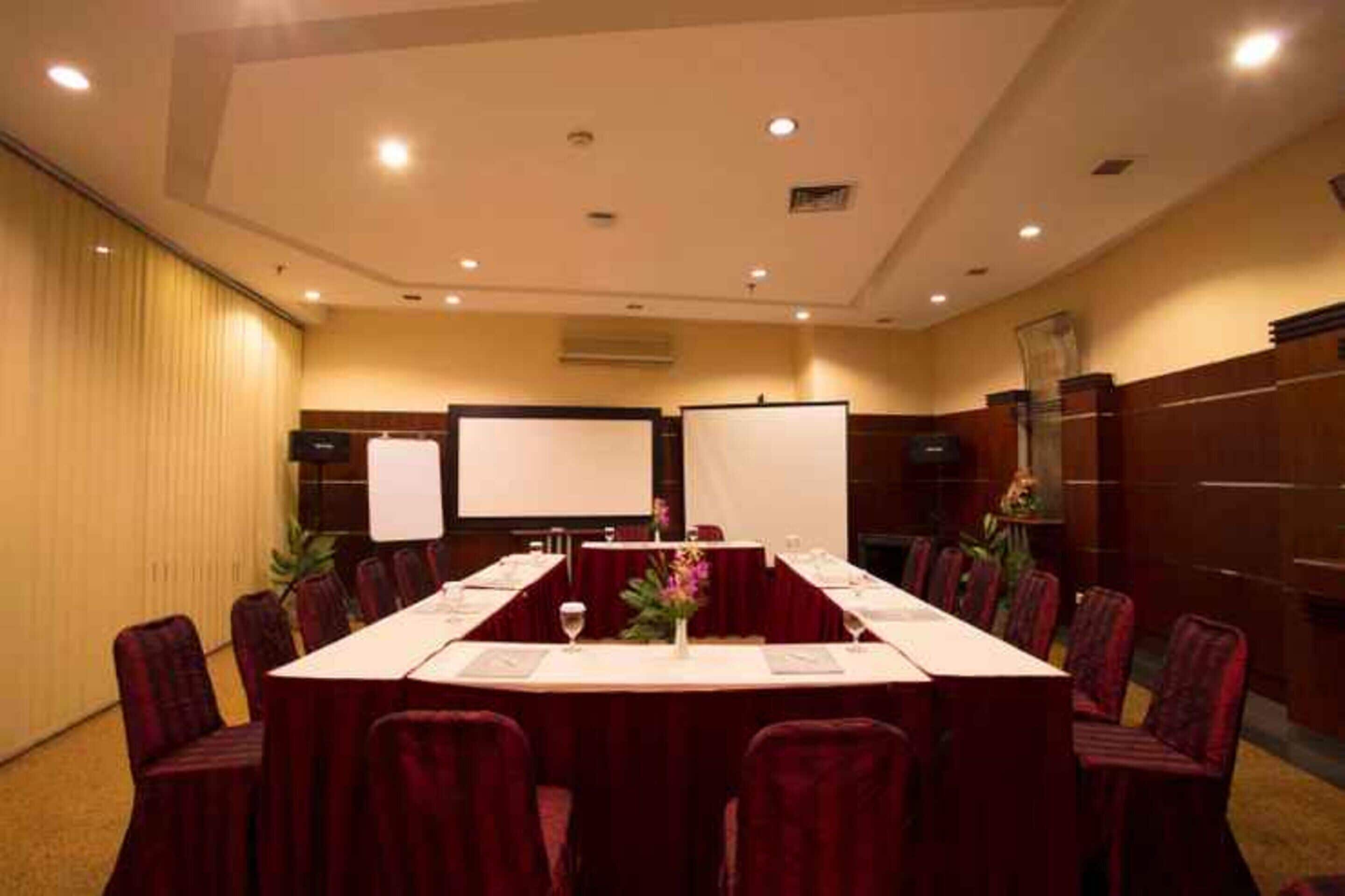 A conference room with a long table, red chairs, a whiteboard, and a projector screen.