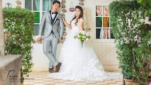 Una pareja vestida de novios está parada frente a un edificio de paredes de piedra con un letrero que dice "Room".