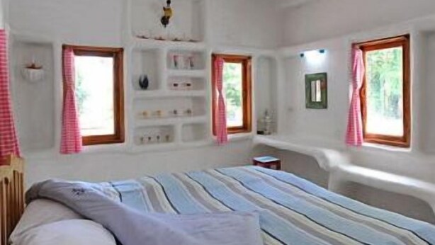 A bedroom with a bed, a shelf unit, and two windows with curtains.