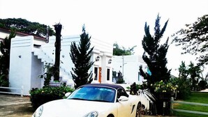 Un coche deportivo blanco estacionado frente a un edificio blanco con escalones y una escalera.